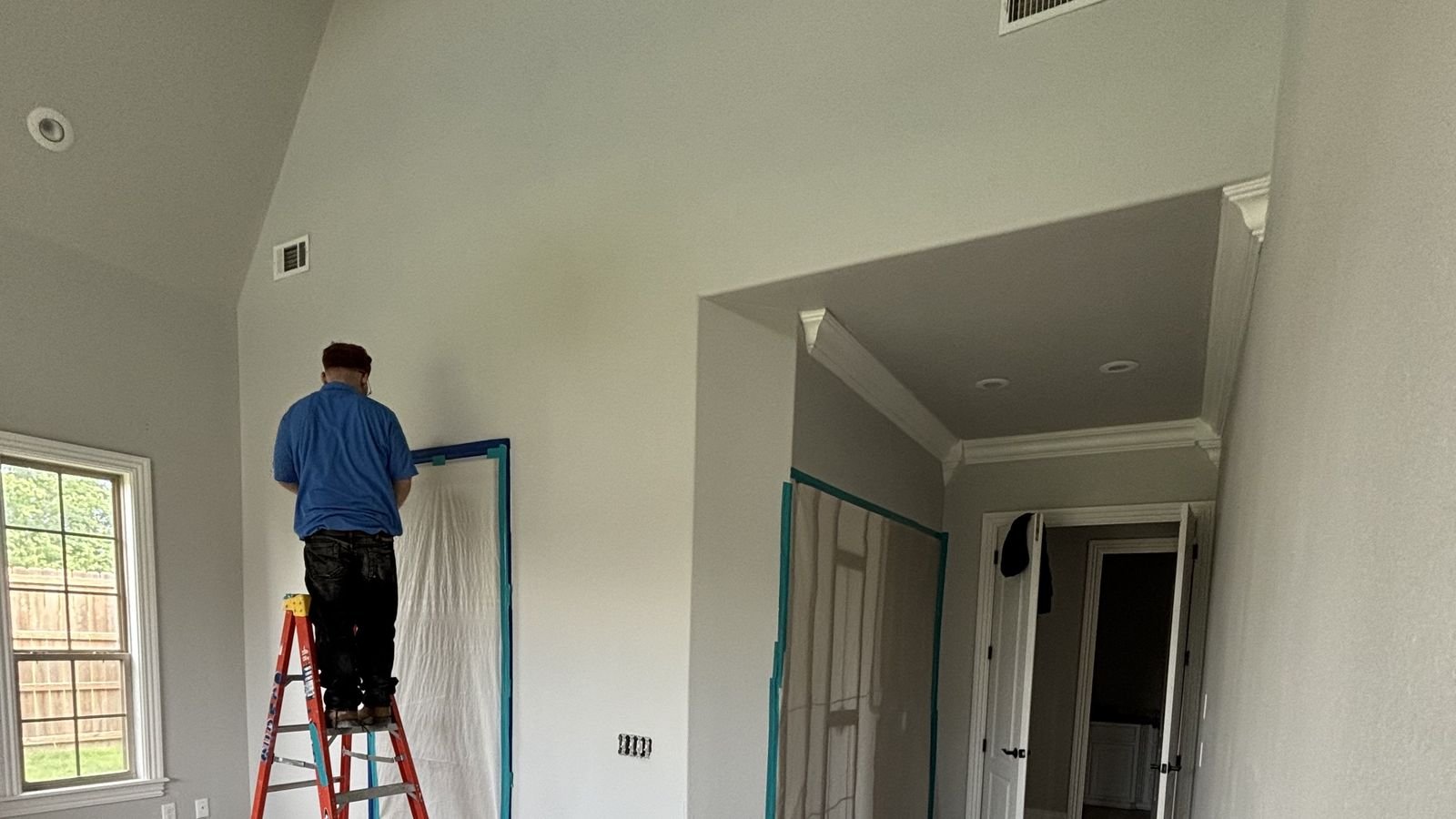 Surfco painter working from a ladder with floors masked and protected in a Northwest Arkansas home